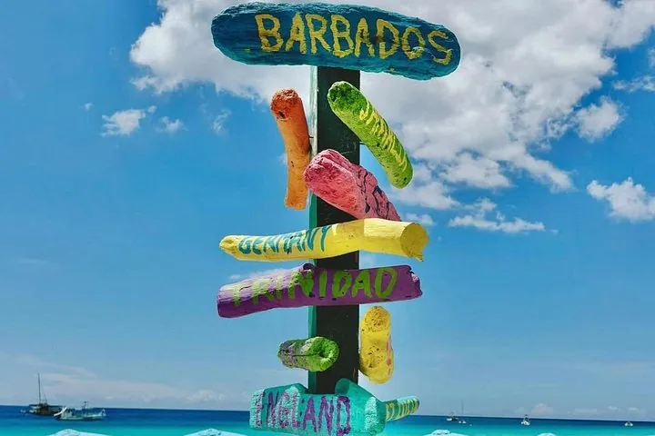 Cartello colorato che indica le direzioni verso vari paesi su una spiaggia.